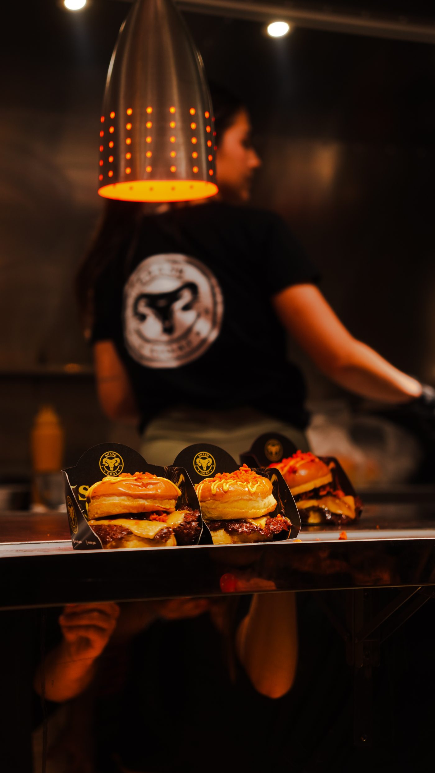Tres hamburguesas de Smash Goat bajo la lámpara de calor de su food truck
