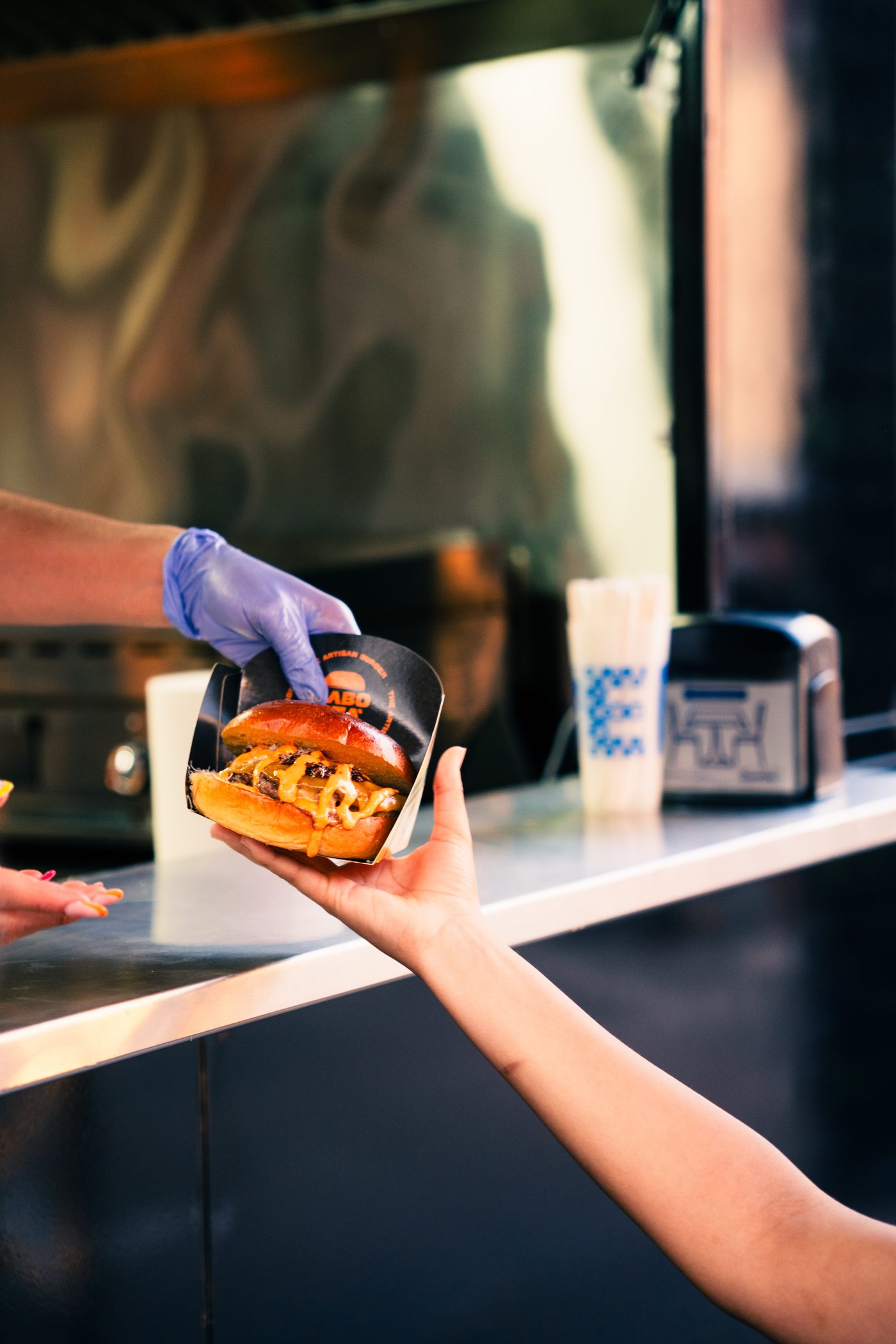 Una hamburguesa pasa de la cocina a la mano del cliente en un food truck del festival