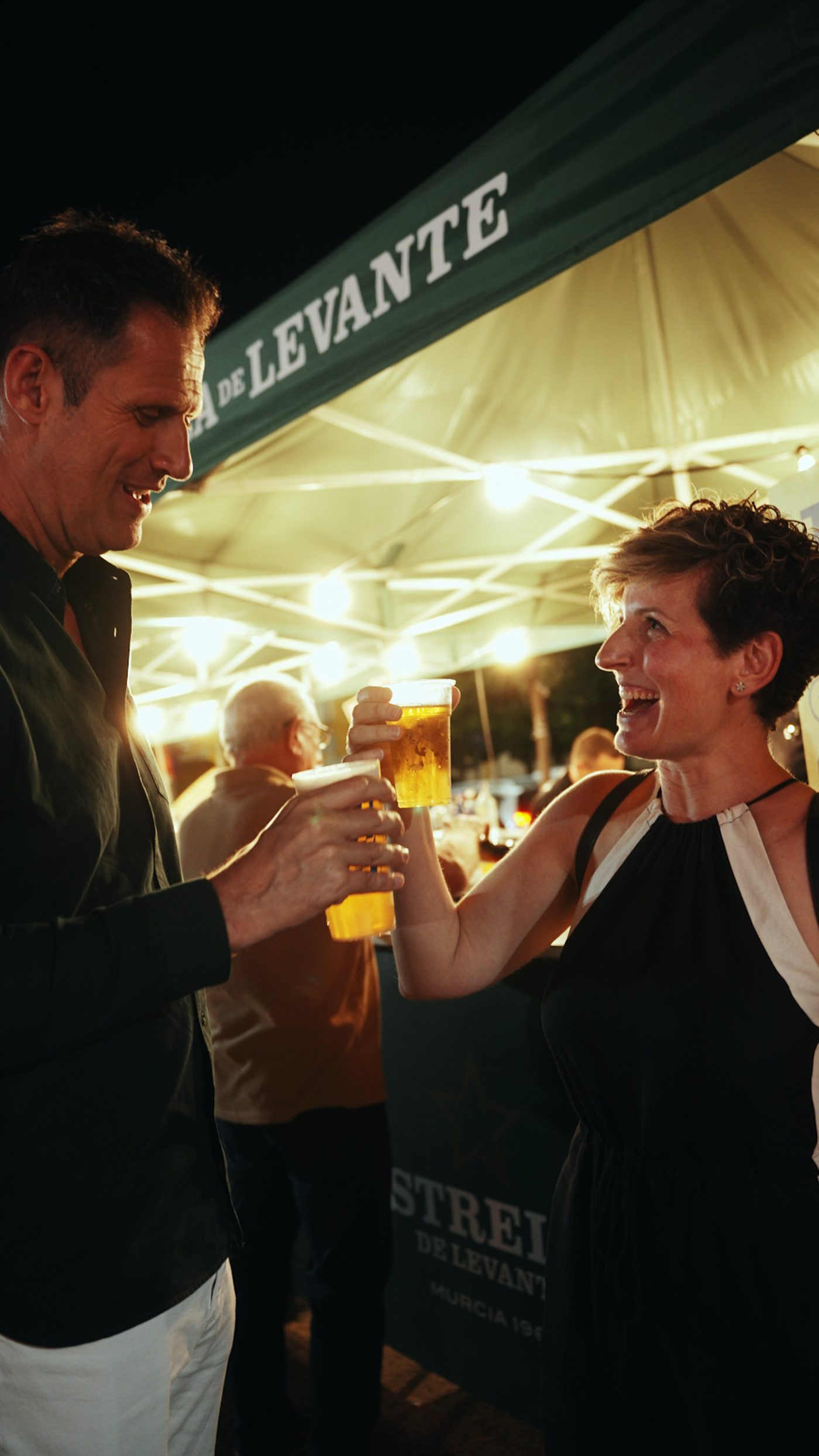 Dos asistentes brindan con cerveza bajo la carpa de Estrella de Levante
